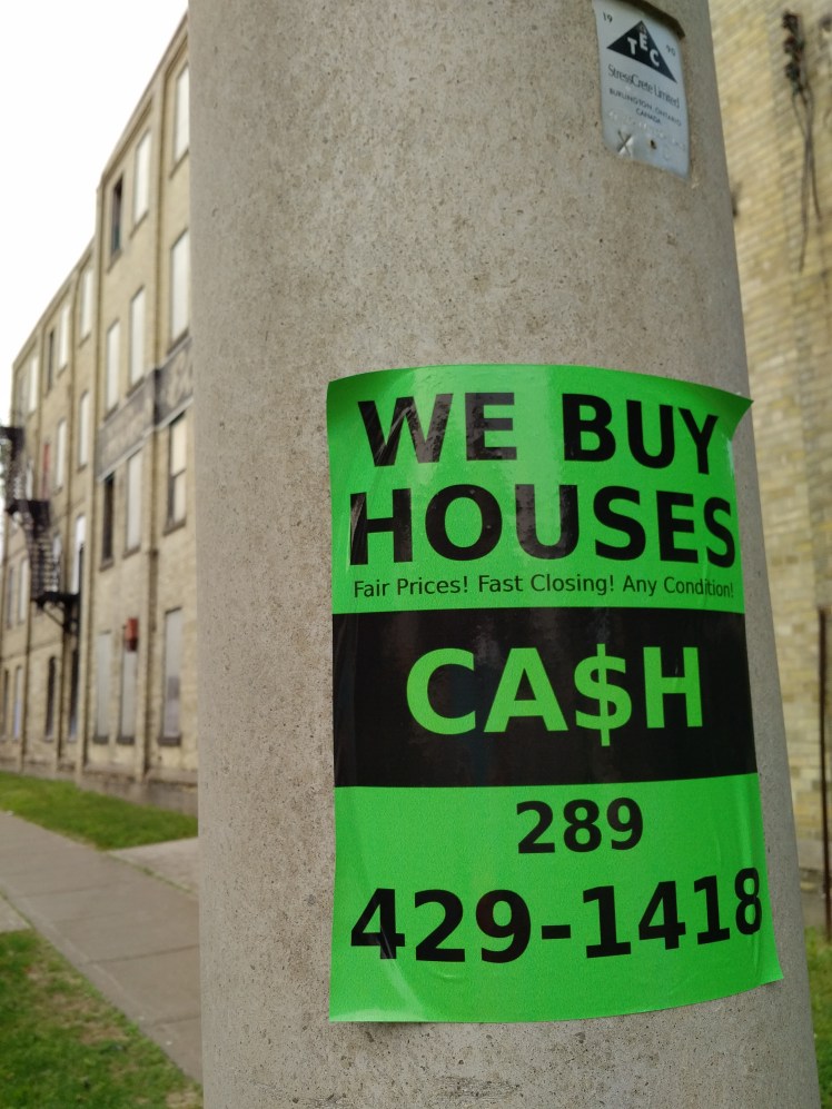 we buy houses sign on a hydro pole in midtown kw