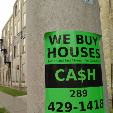 we buy houses sign on a hydro pole in midtown kw