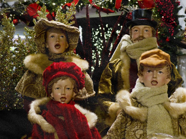 Figures in coats and scarves singing Christmas carols outdoors. 